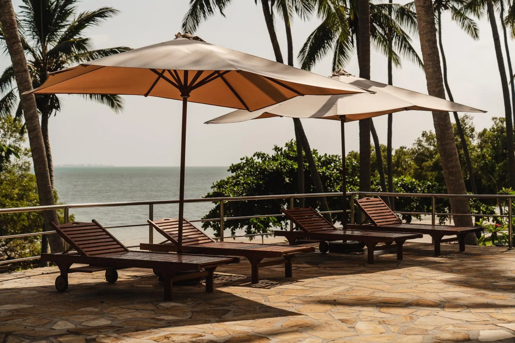 Transats en bois sous des parasols sur une terrasse ensoleillée avec vue sur la mer.