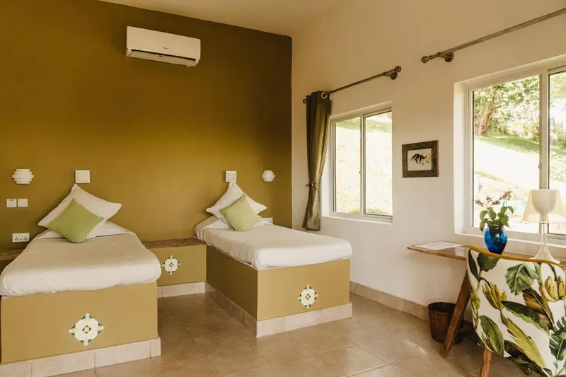 Chambre lumineuse avec deux lits simples et une vue sur la végétation.
