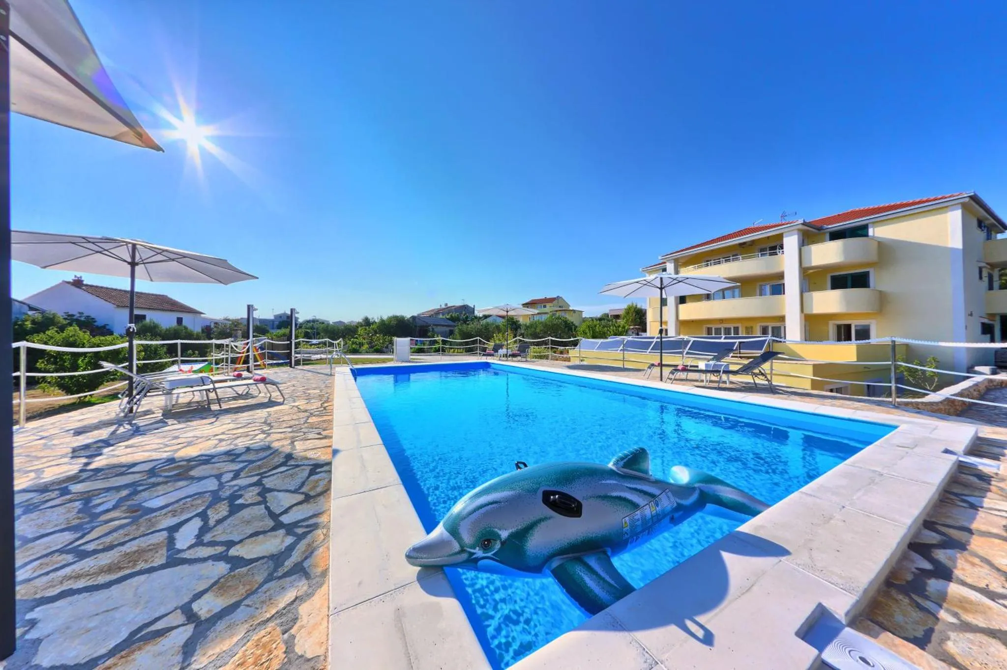 Une piscine rectangulaire avec un dauphin gonflable, entourée d'une terrasse pavée et de transats.