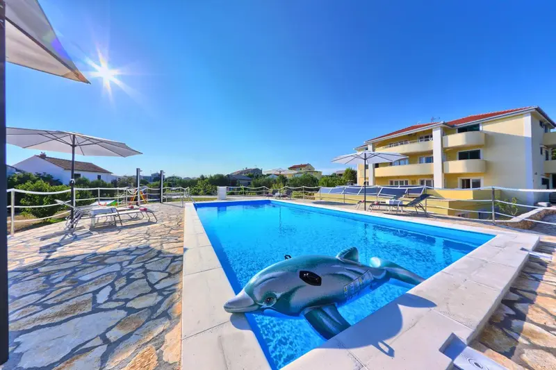 Une piscine rectangulaire avec un dauphin gonflable, entourée d'une terrasse pavée et de transats.