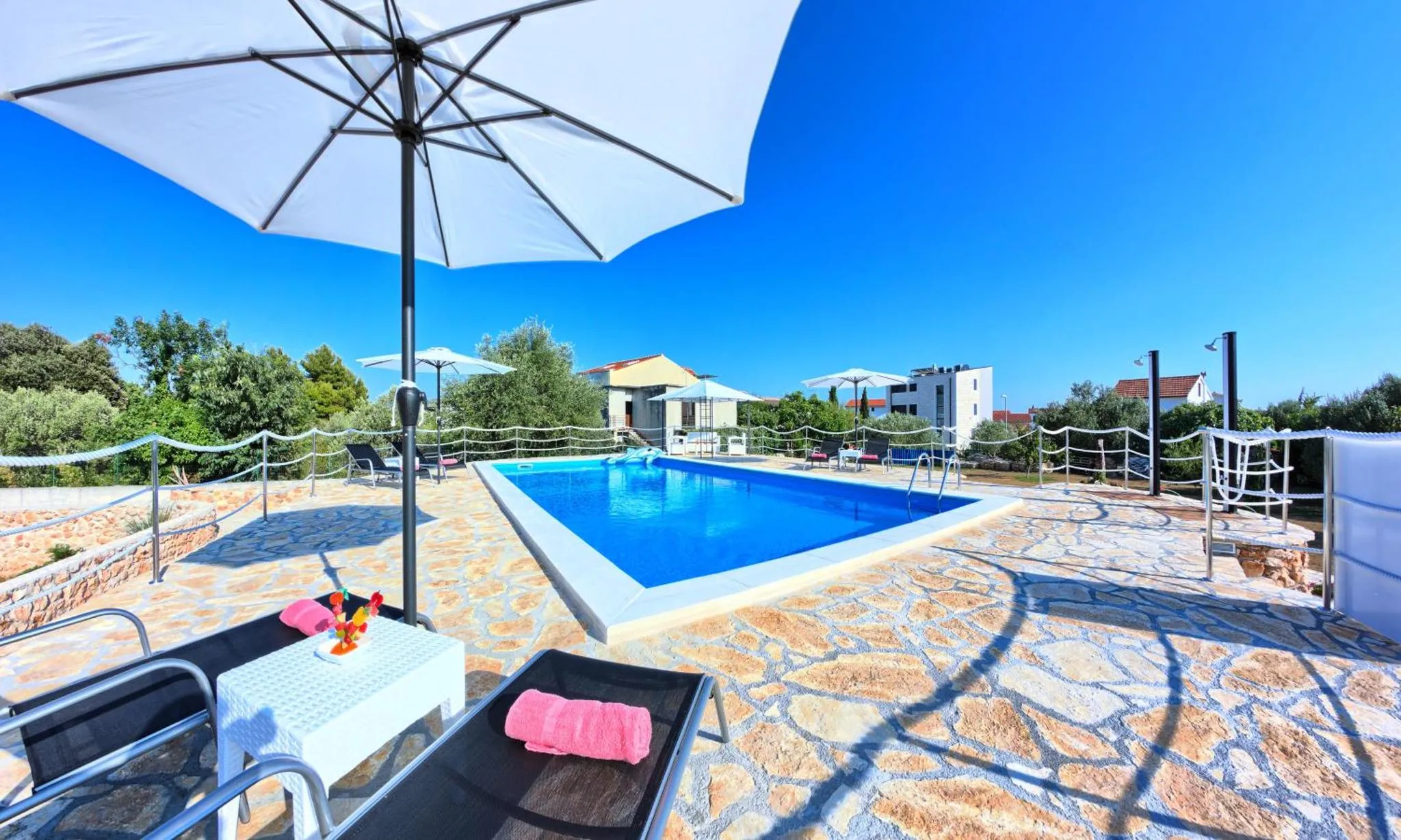 Une piscine rectangulaire bordée d'une terrasse carrelée avec des transats et des parasols.