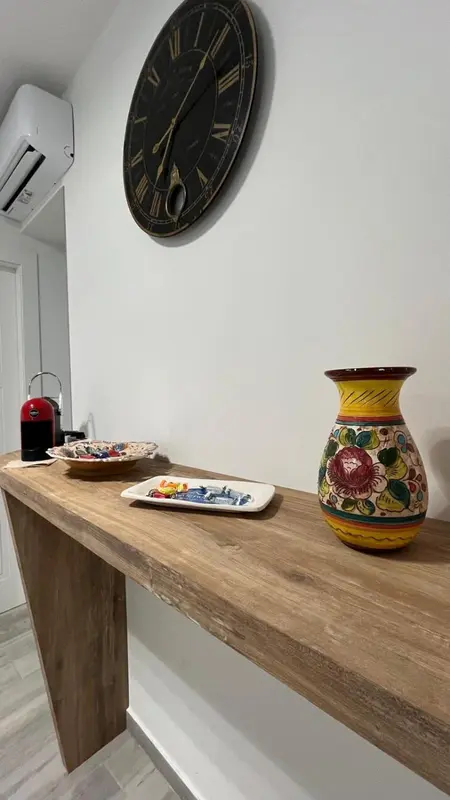Une étagère en bois présente une machine à café, des assiettes décorées et un vase coloré.