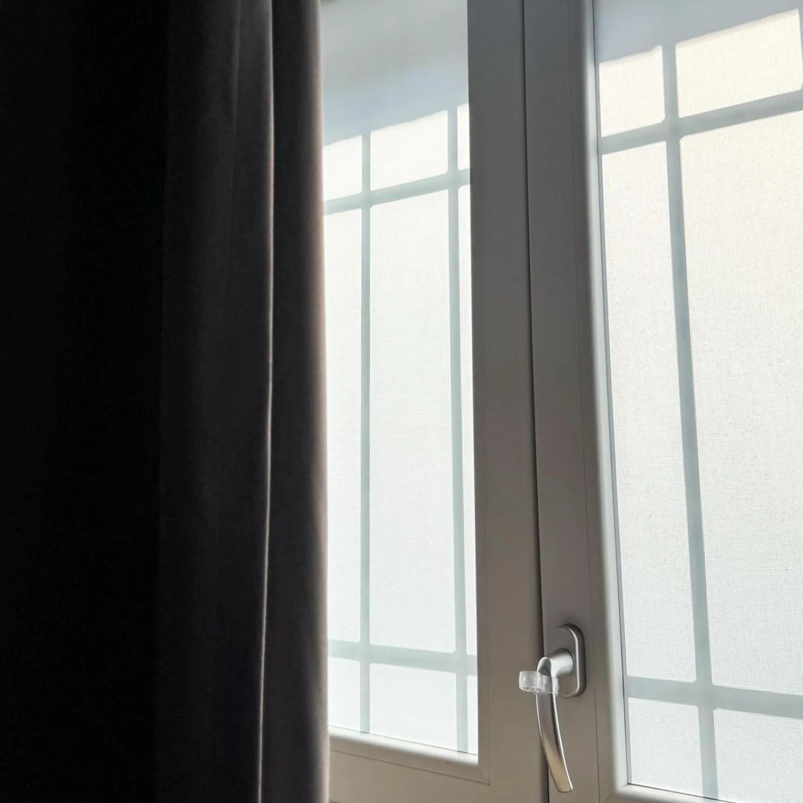 Rideau sombre et fenêtre à carreaux ouverte.