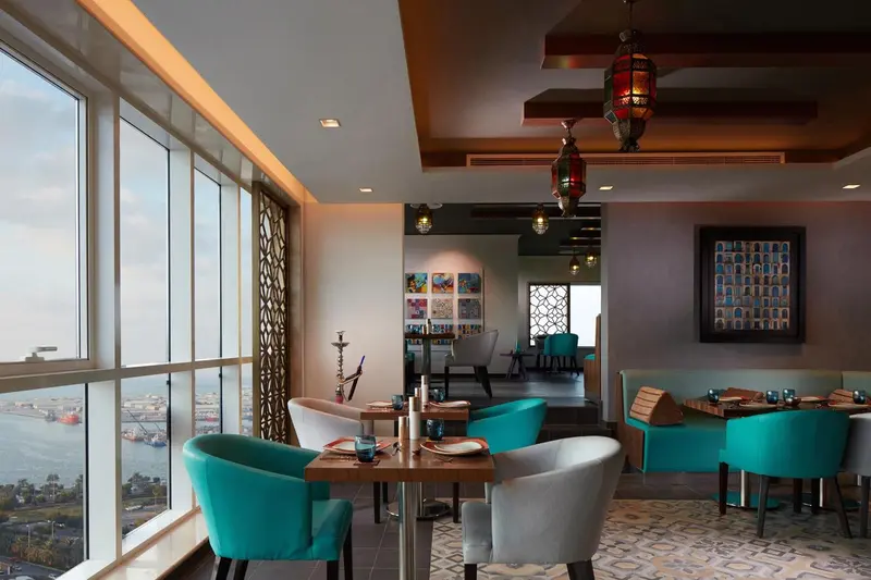 Une salle de restaurant lumineuse avec des tables dressées et une vue sur la mer.