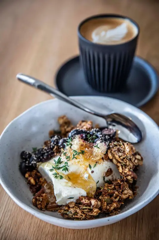 Un bol de granola aux fruits et une tasse de café sur une table en bois.