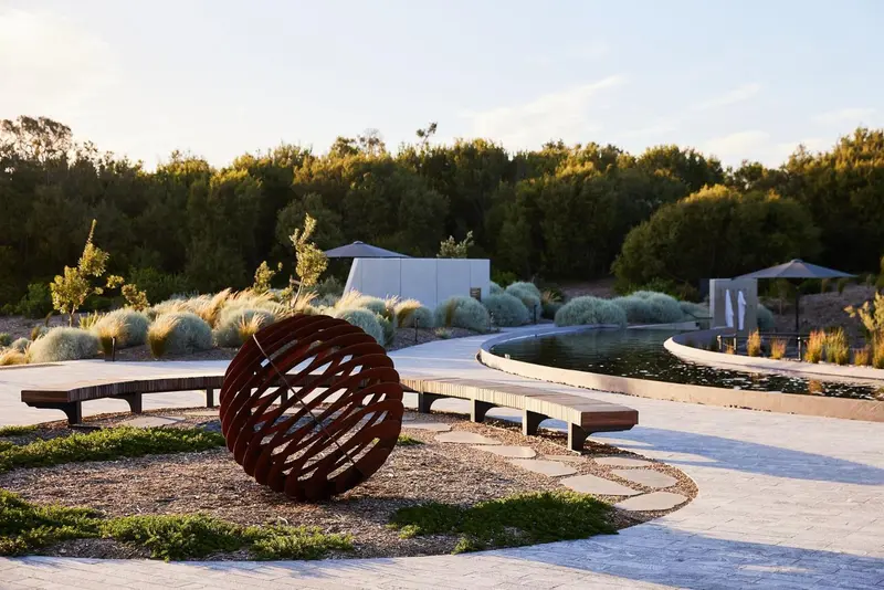 Un jardin paysager avec des sculptures métalliques et des bancs en pierre.