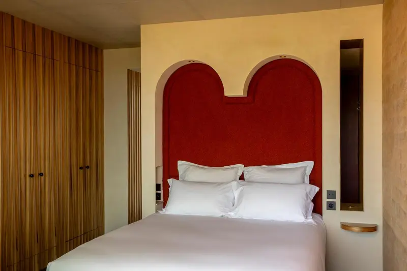 Une chambre à coucher avec un lit recouvert de draps blancs et une tête de lit rouge.
