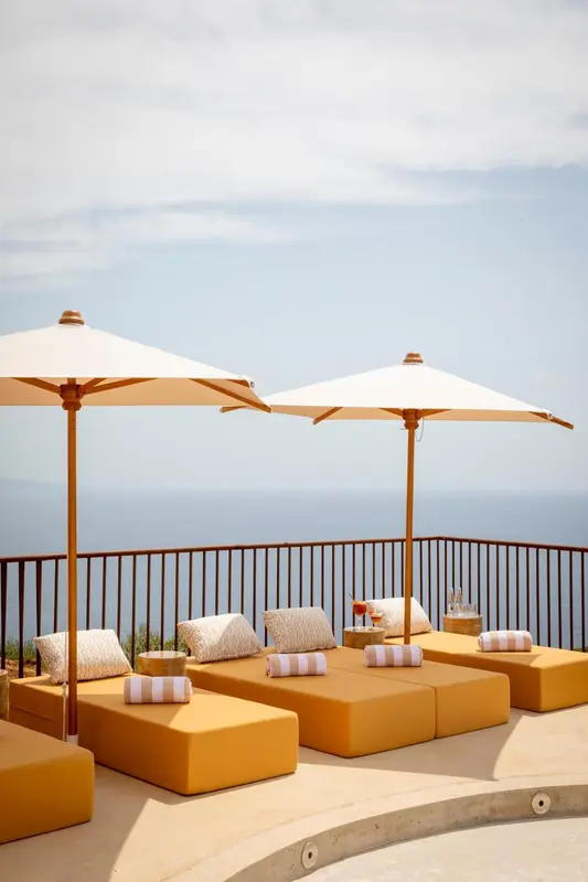 Transats orange sous des parasols sur une terrasse avec vue sur la mer.
