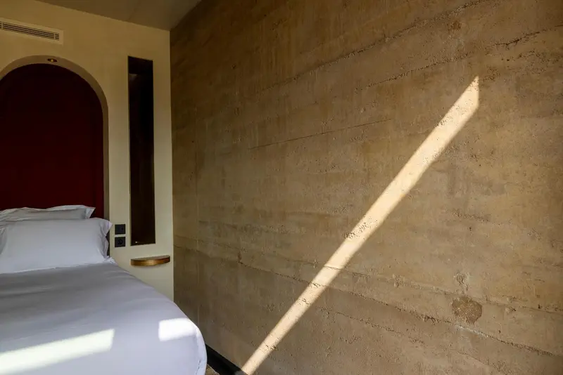 Une chambre lumineuse avec un lit blanc et un mur texturé.