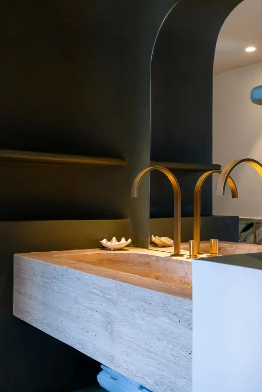 Un lavabo moderne en pierre avec des robinets dorés est visible dans une salle de bain.