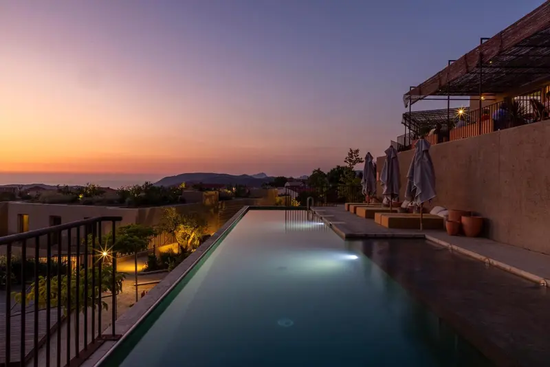 Une piscine à débordement surplombe un paysage côtier au coucher du soleil.
