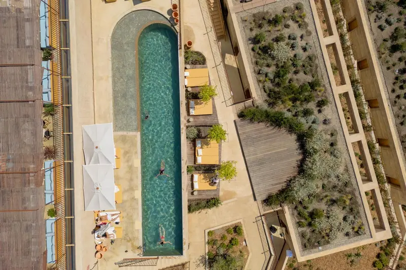 Vue aérienne d'une piscine rectangulaire entourée de terrasses aménagées et de végétation.