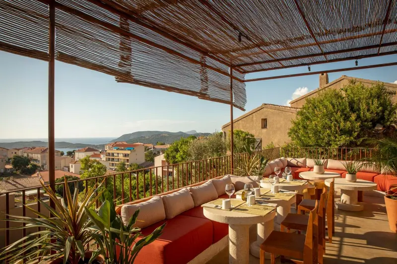 Terrasse ombragée avec tables et canapés donnant sur une vue panoramique.