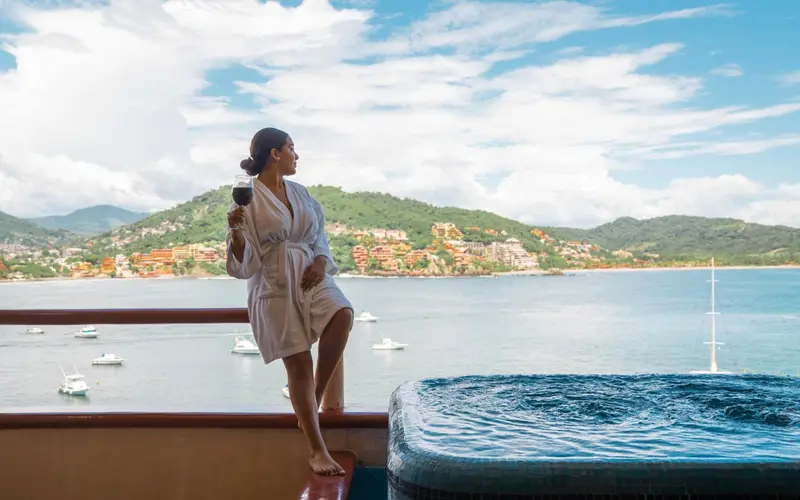 Une femme en peignoir admire la vue sur la mer depuis un balcon avec jacuzzi.