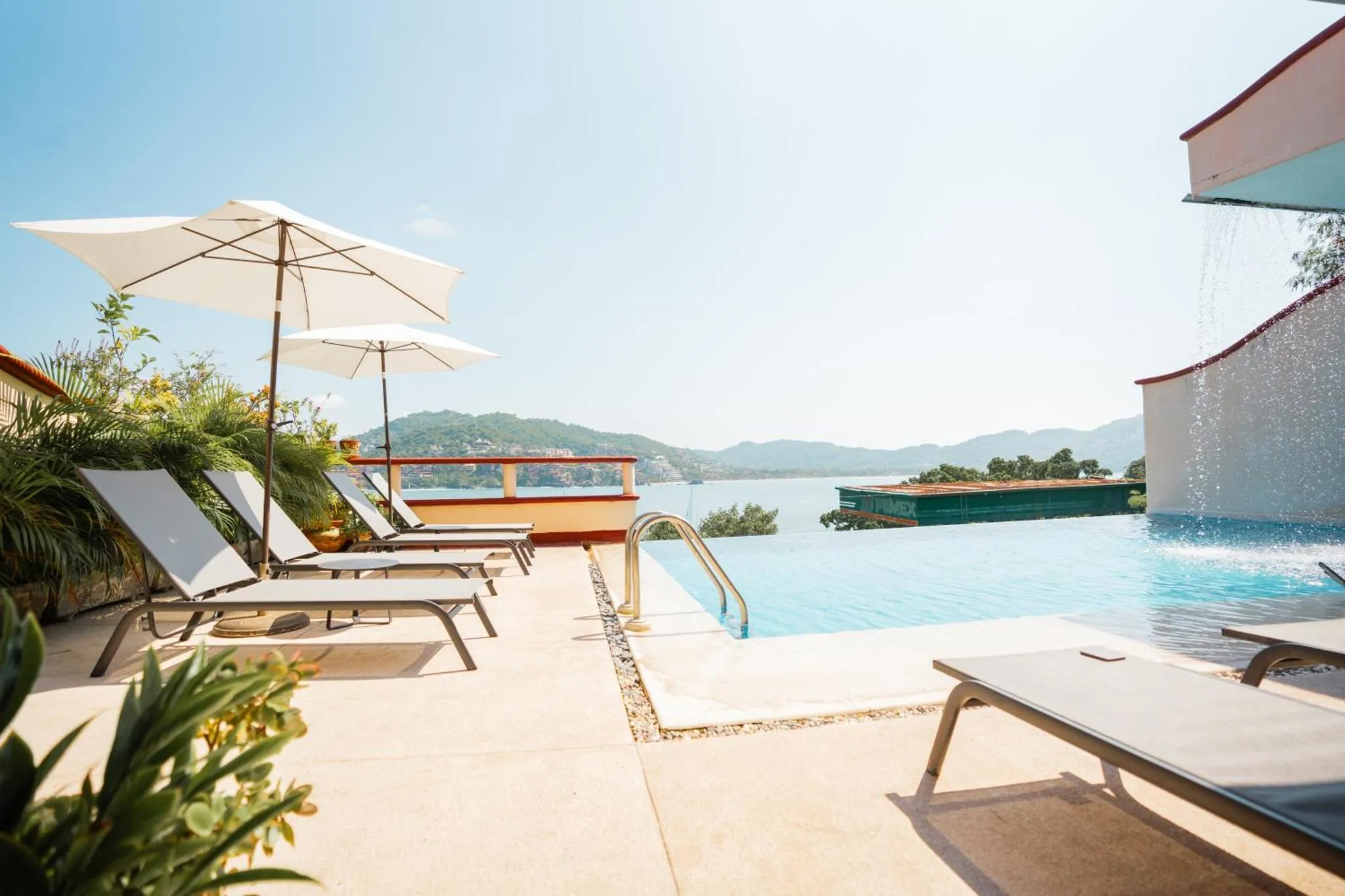 Transats blancs disposés au bord d'une piscine à débordement avec vue sur la mer.