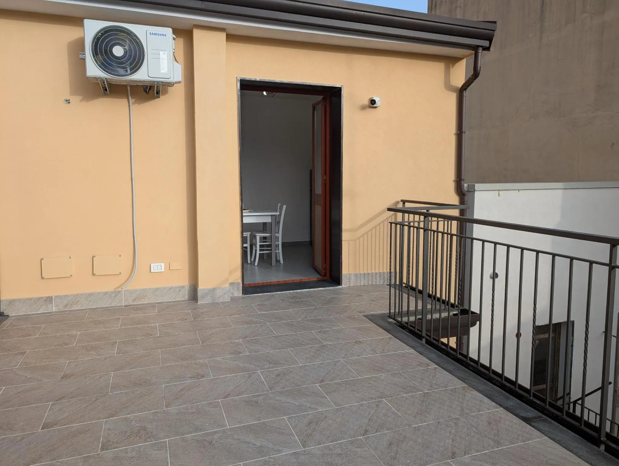 Terrasse carree pavee donnant sur une piece avec table et chaises.