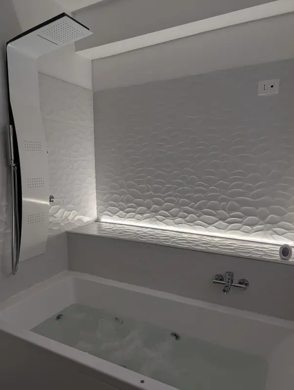 Une baignoire blanche est visible dans une salle de bain moderne aux murs texturés.