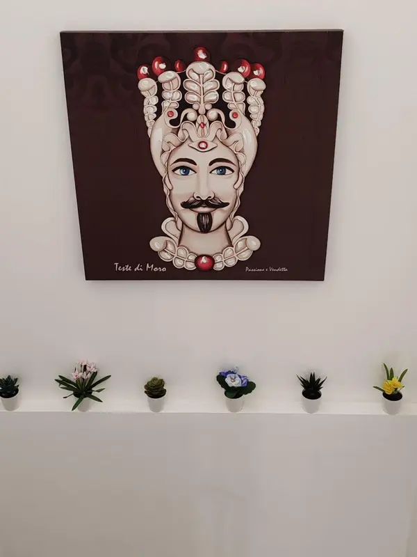 Portrait stylisé d'un visage orné d'une coiffe élaborée, accroché au mur au-dessus d'une étagère avec des plantes.