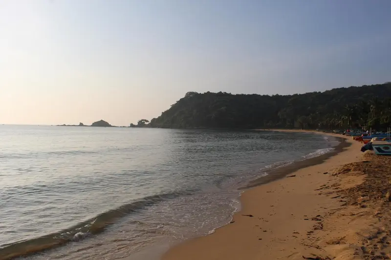 Une plage de sable fin borde une mer calme sous un ciel clair.