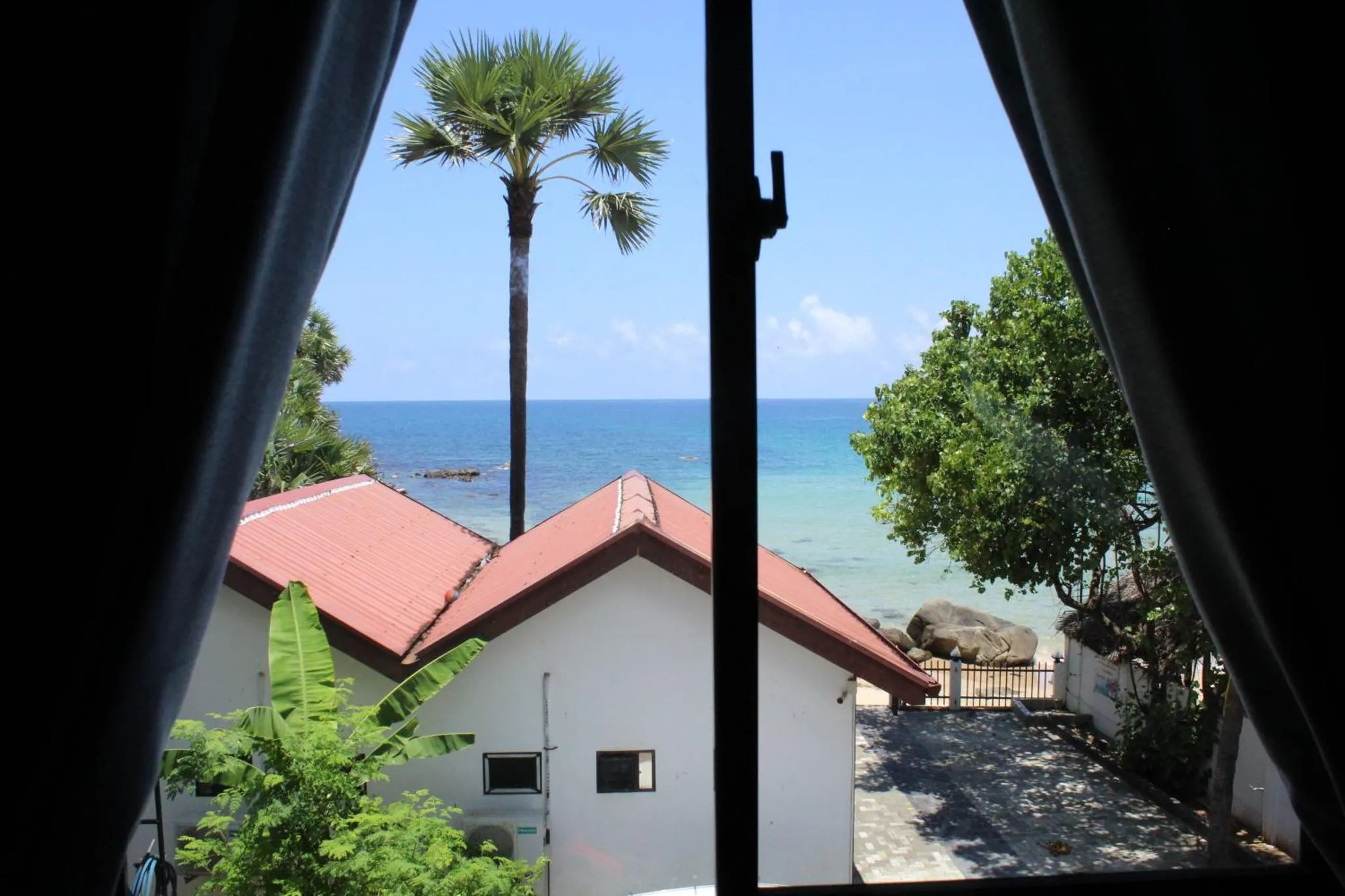 Vue sur la mer et les toits depuis une fenêtre ombragée.