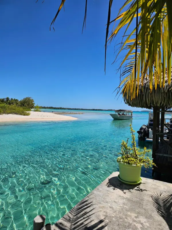 Vue sur une eau turquoise et une plage de sable blanc depuis un ponton ombragé.