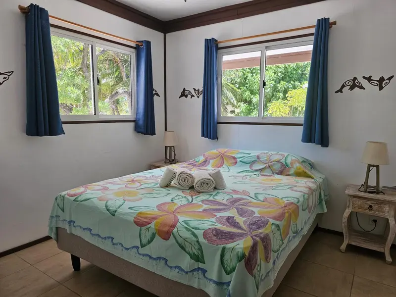 Une chambre lumineuse avec un lit recouvert d'une courtepointe fleurie et des rideaux bleus.