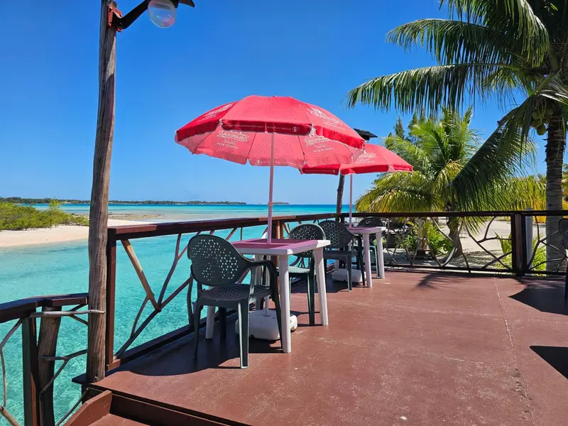 Terrasse avec tables et parasols donnant sur une plage turquoise.