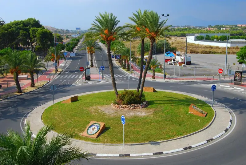 Vue aérienne d'une avenue bordée de palmiers menant à un rond-point.