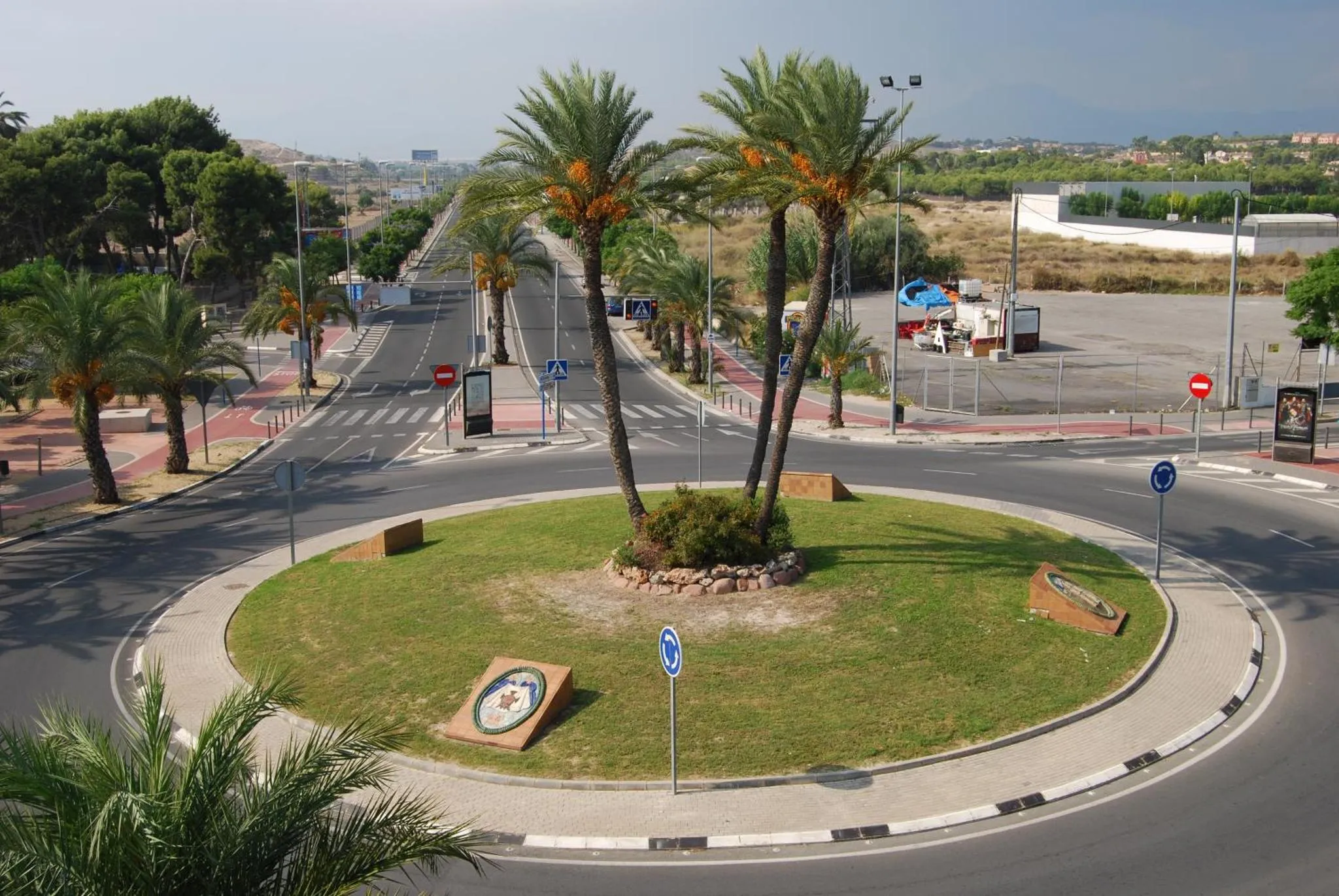 Vue d'une avenue bordée de palmiers menant à un rond-point.