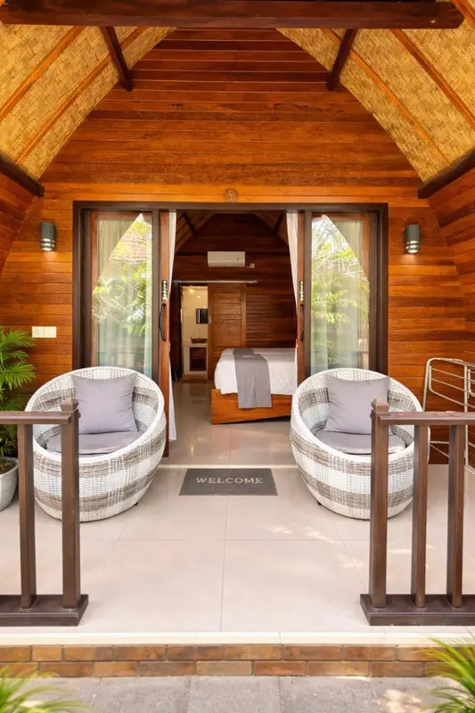 Terrasse en bois devant une chambre avec deux fauteuils en osier.