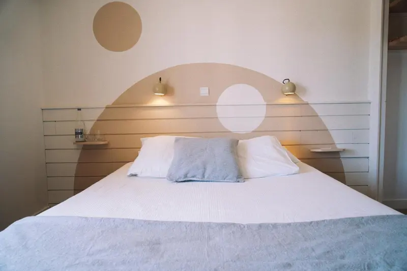 Un lit double blanc avec des oreillers gris dans une chambre décorée de formes géométriques.