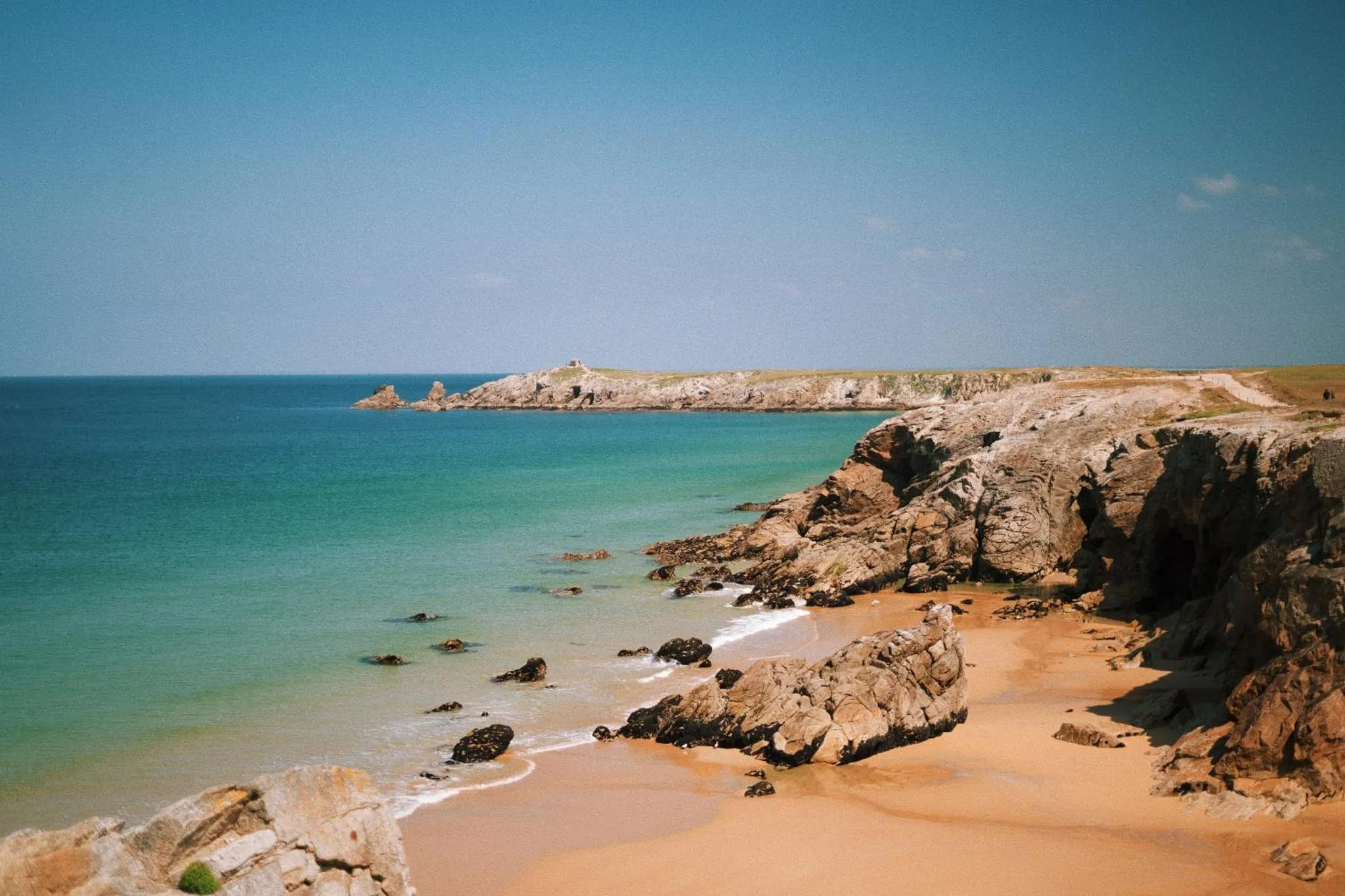 Une plage de sable fin bordée d'une eau turquoise et de formations rocheuses.