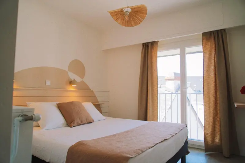 Une chambre lumineuse avec un lit double et un accès à un balcon.