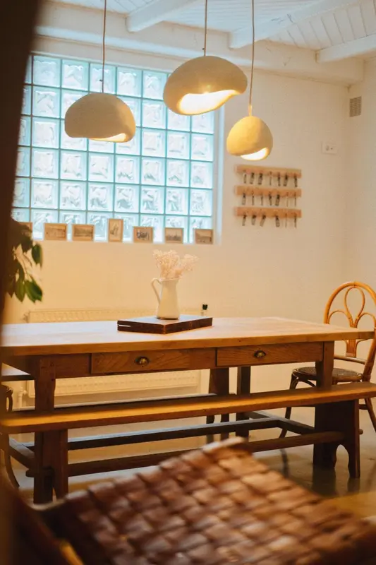 Une table en bois est mise en valeur par des luminaires suspendus et un mur en briques de verre.