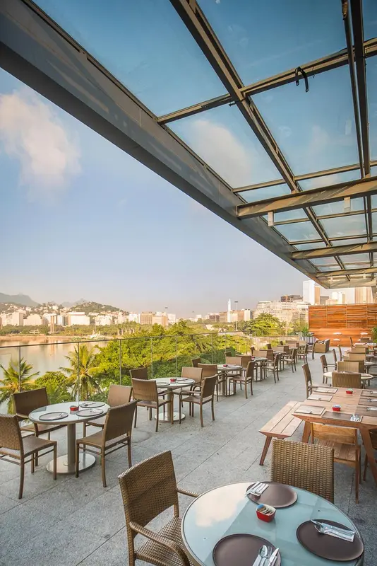Terrasse ombragée avec tables et chaises donnant sur une vue urbaine et verdoyante.