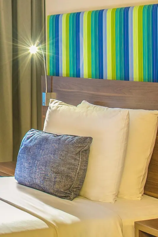 Un lit avec des oreillers blancs et un coussin bleu est contre une tête de lit rayée.