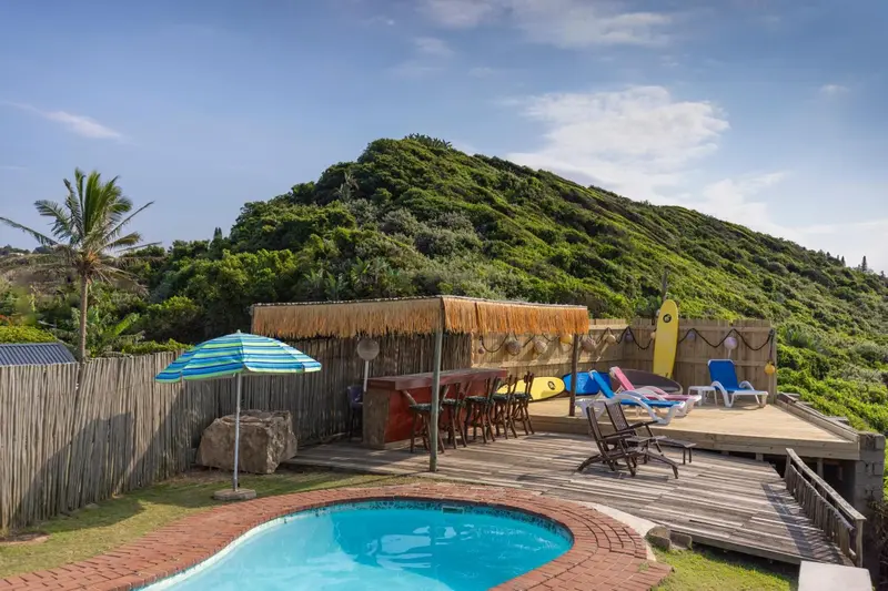 Terrasse en bois avec mobilier de jardin et piscine devant une colline verdoyante.