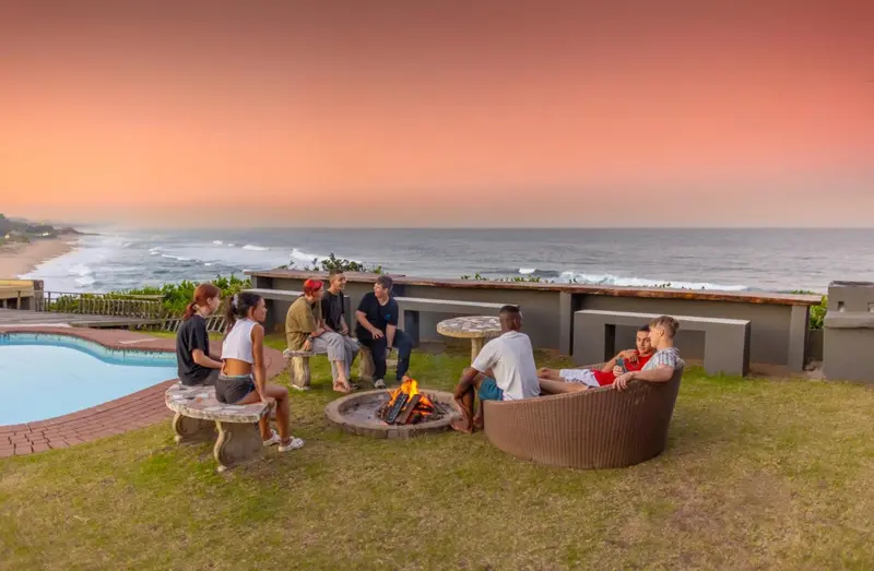 Un groupe de personnes est assis autour d'un feu de camp avec vue sur la mer.
