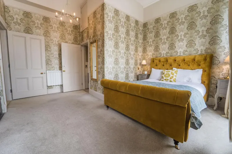 Une chambre lumineuse avec un grand lit recouvert d'une courtepointe jaune et de coussins.