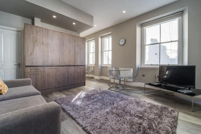 Interieur clair avec canape, table et telévision devant une grande fenêtre.