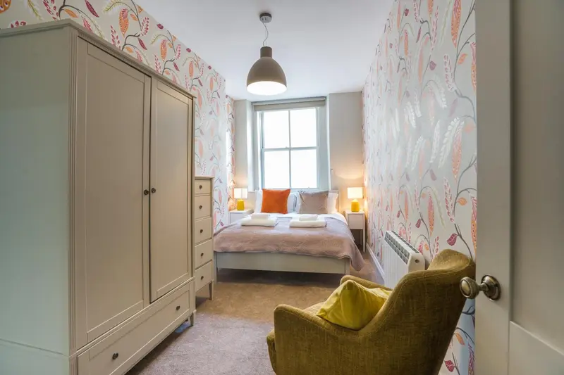 Une chambre lumineuse avec un lit fait et un fauteuil jaune.