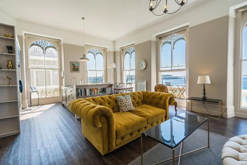 Un salon lumineux avec un canapé jaune et une vue sur la mer.
