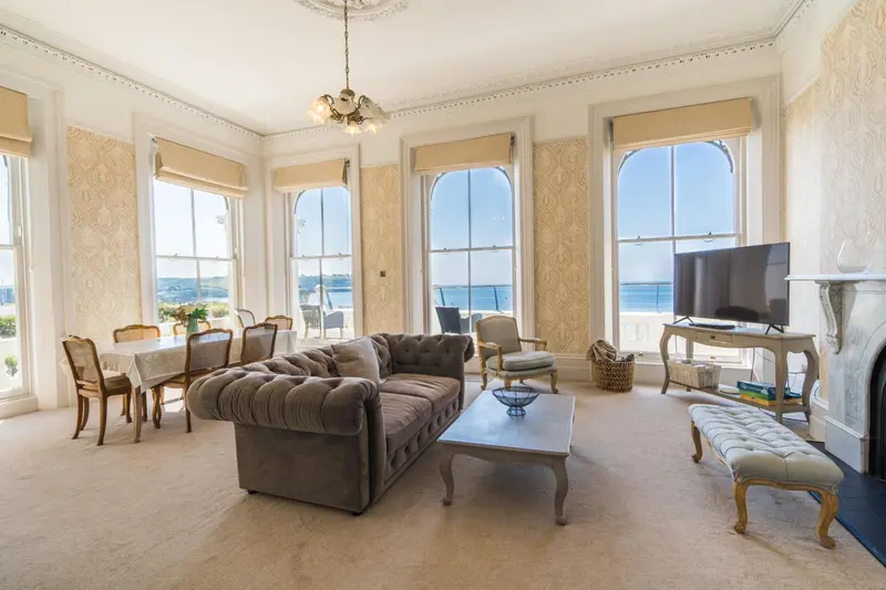 Un salon lumineux avec canapés et table à manger offre une vue sur la mer.