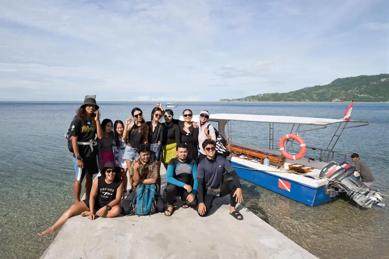 Groupe de personnes souriantes posant sur un quai devant un bateau bleu et blanc.