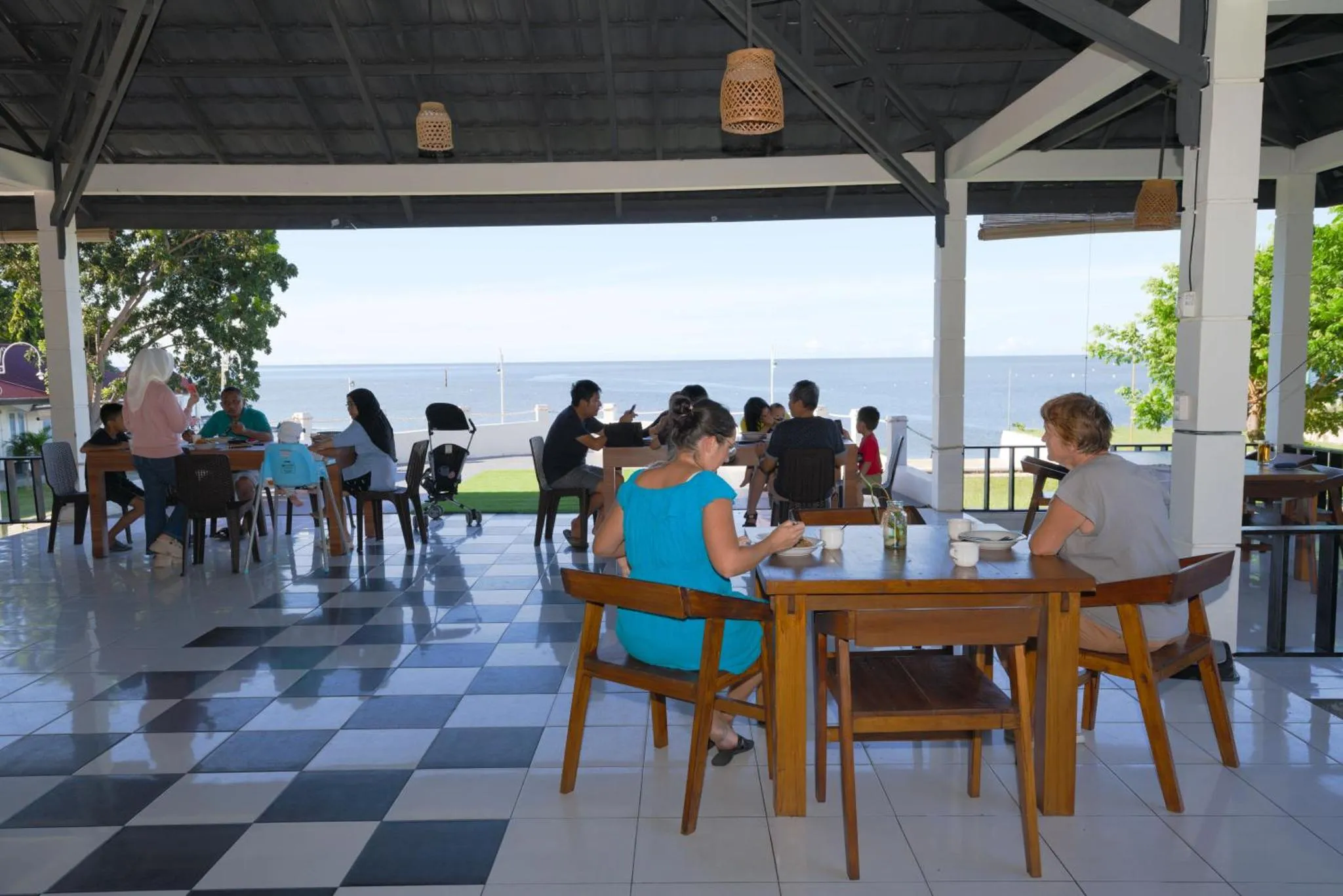 Des clients déjeunent à des tables en bois sur une terrasse carrelée face à la mer.