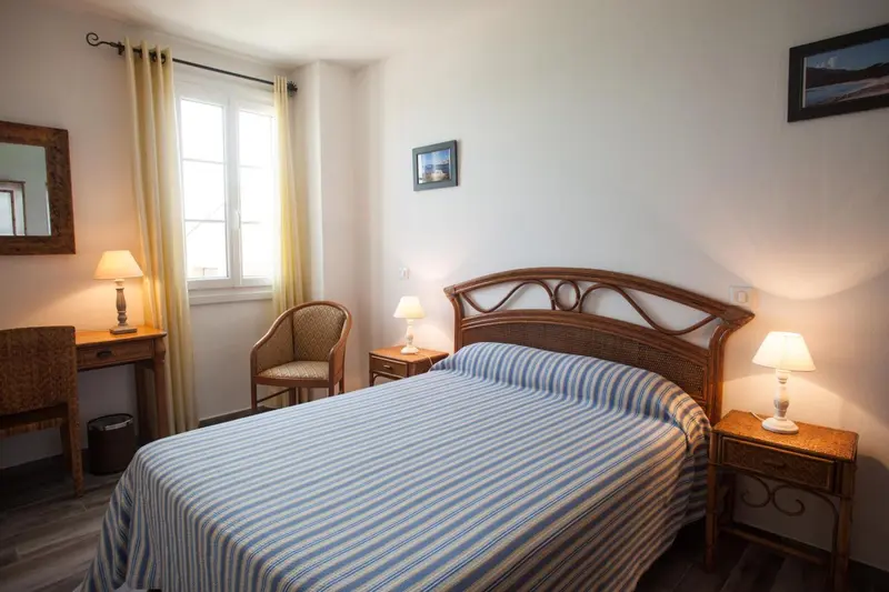 Une chambre lumineuse avec un lit recouvert d'une couette à rayures et une chaise en rotin.