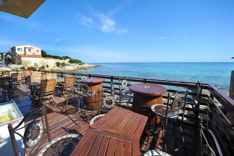 Terrasse en bois avec tables et chaises donnant sur la mer.