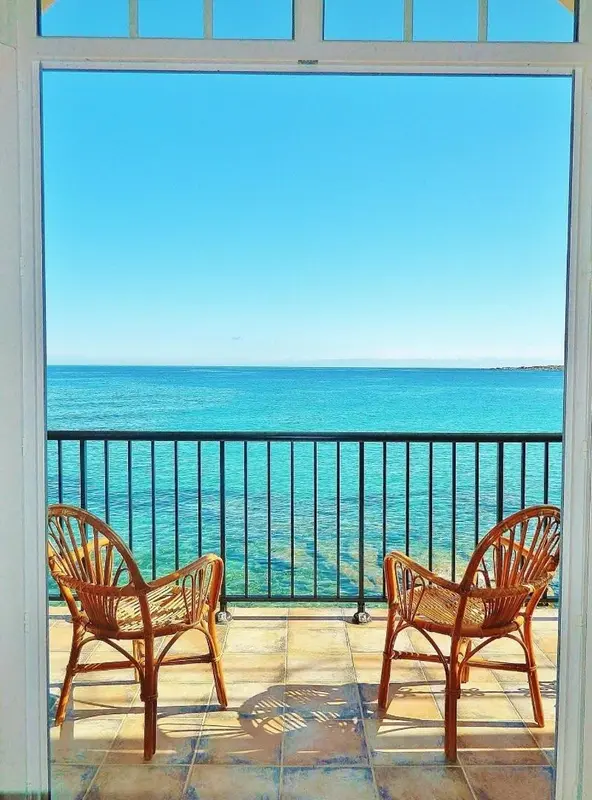 Deux fauteuils en osier sur une terrasse carrelée donnant sur la mer.