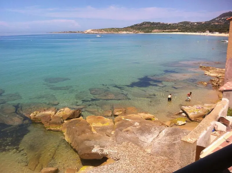 Vue sur une plage de sable fin et une mer turquoise depuis un promontoire rocheux.