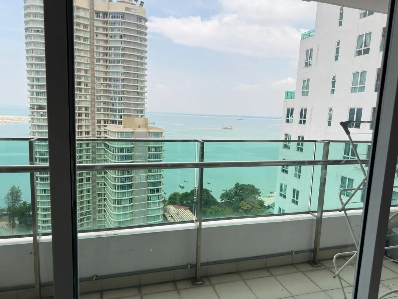 Vue d'une terrasse avec une rambarde en verre donnant sur la mer et des bâtiments.